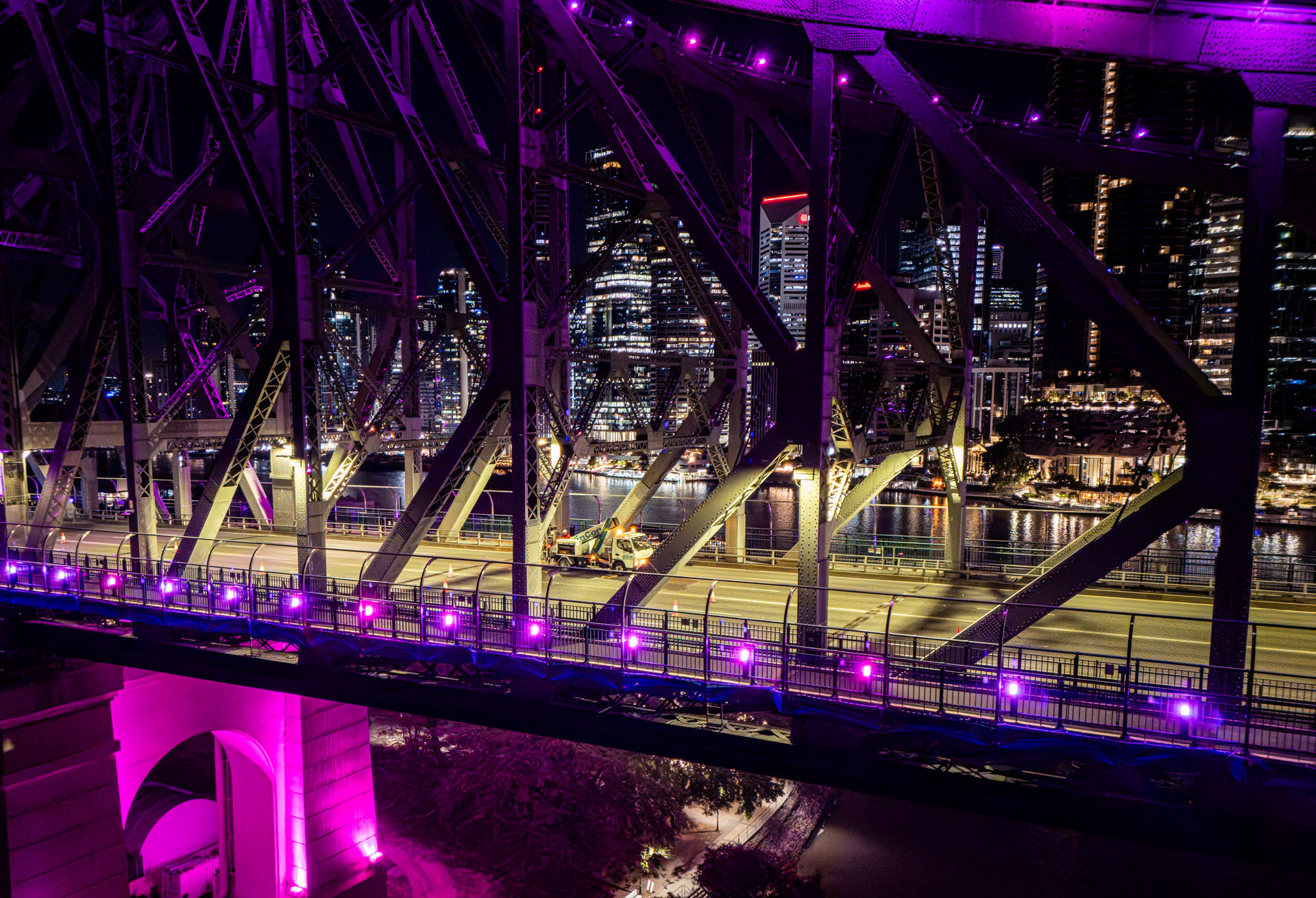 Side aerial perspective of Story Bridge structure illuminated at night during live maintenance operations.
