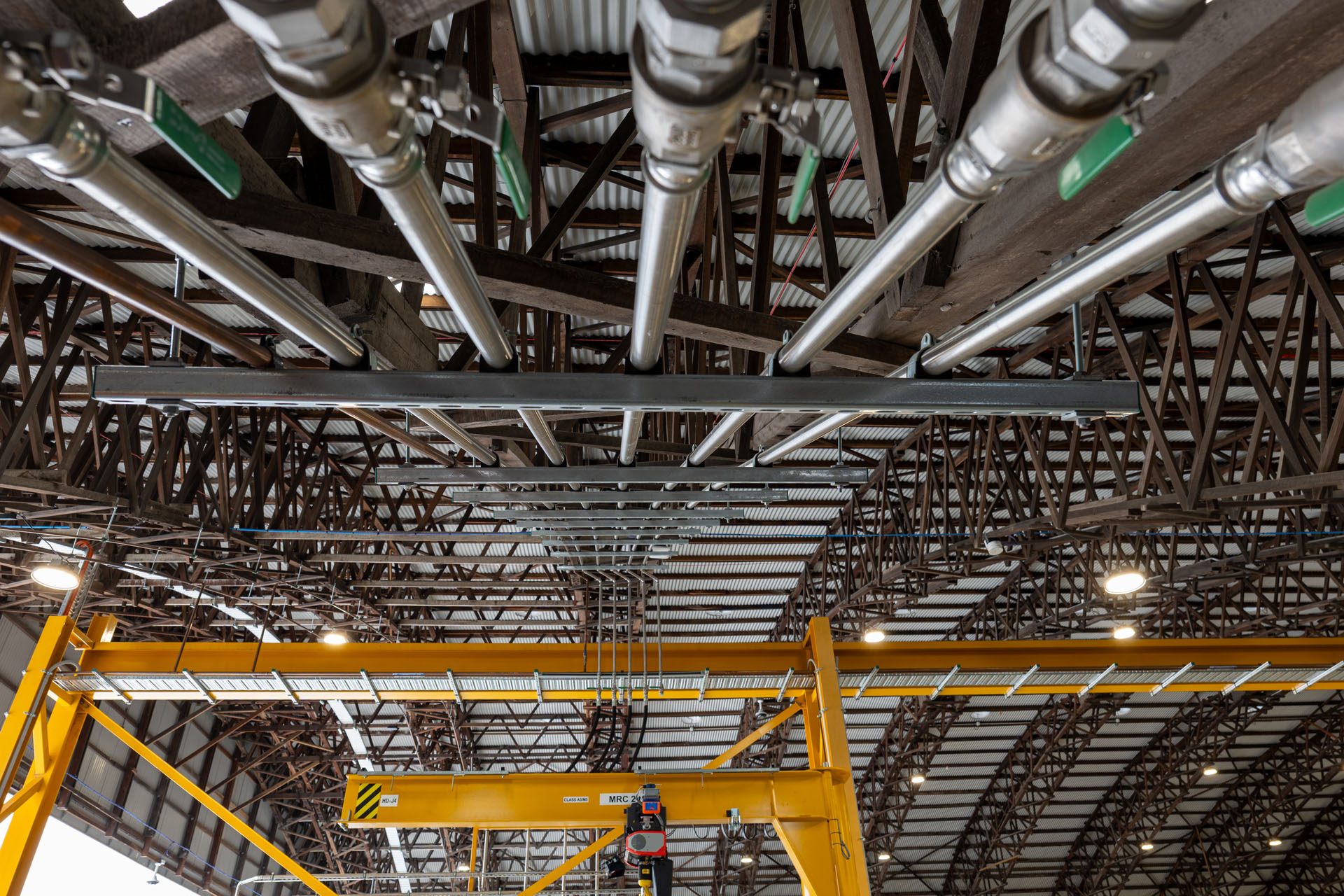 Symmetrical overhead plumbing and service pipe systems inside heavy equipment workshop in Archerfield, QLD.